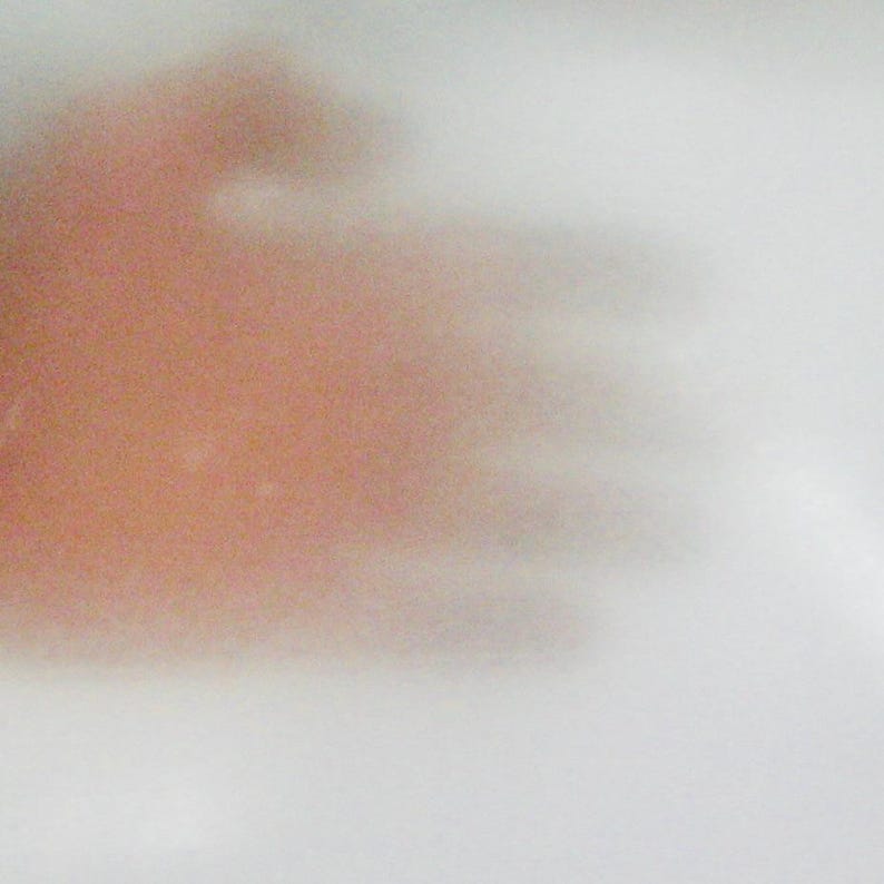 May include: A translucent white material with a soft, blurred, and indistinct reddish-orange shape visible behind the surface. The texture appears smooth and thin, creating a diffused effect that obscures the details of the object behind it.