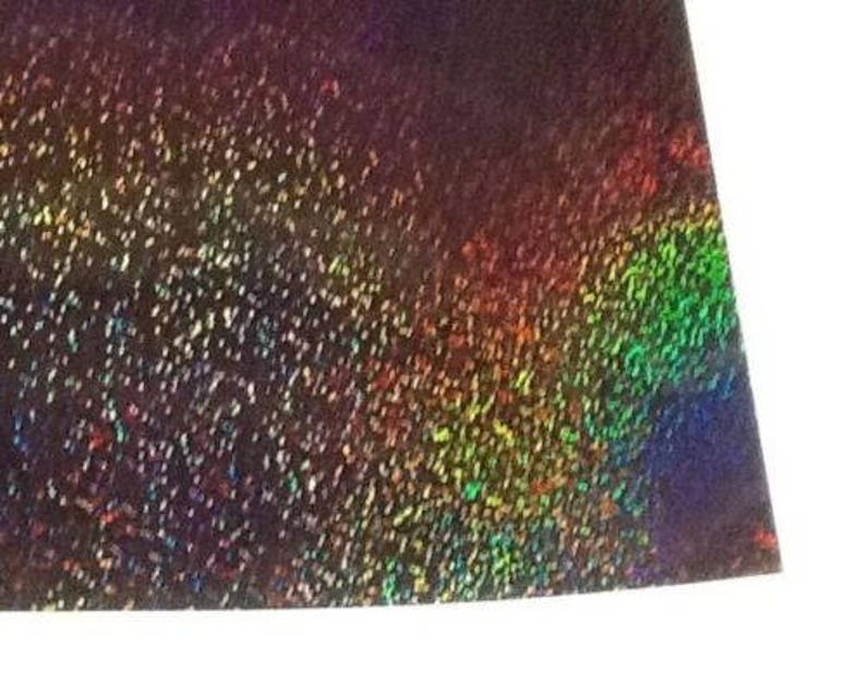 May include: A sheet of iridescent holographic paper with a dark purple base and a rainbow sheen. The paper has a speckled texture.