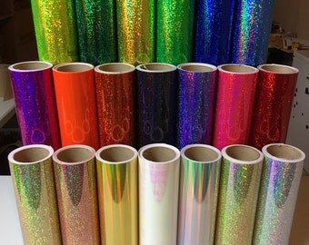 Pode incluir: Uma coleção de vinte rolos cilíndricos de vinil adesivo dispostos em três filas. Os rolos apresentam vários acabamentos, incluindo holográficos, com glitter e cores metálicas sólidas como lima, verde, azul, laranja, vermelho, rosa, ouro e prata.