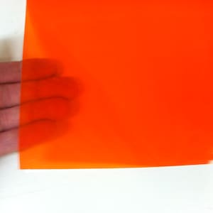 May include: A rectangular sheet of translucent orange plastic film with a smooth, glossy surface. The material is semi-transparent, allowing light to pass through while maintaining a vibrant, solid orange color across the entire flat surface.