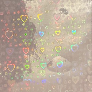 Puede incluir: Hoja hologr&aacute;fica con un patr&oacute;n de corazones y c&iacute;rculos. Los corazones son de varios tama&ntilde;os y colores, incluyendo rosa, amarillo y azul. El fondo es de color plata claro.