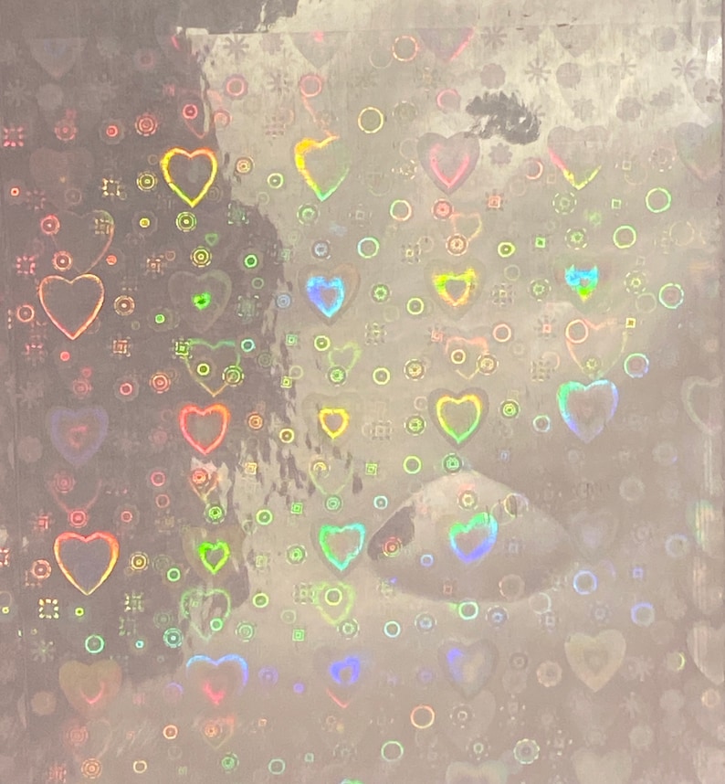 Puede incluir: Hoja hologr&aacute;fica con un patr&oacute;n de corazones y c&iacute;rculos. Los corazones son de varios tama&ntilde;os y colores, incluyendo rosa, amarillo y azul. El fondo es de color plata claro.
