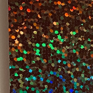 May include: Close-up of iridescent holographic fabric with a gradient of colours, including red, orange, green, blue, and purple. The fabric is made of small, round sequins that create a shimmering effect.