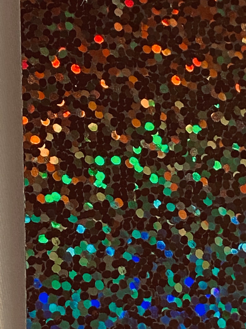 May include: Close-up of iridescent holographic fabric with a gradient of colours, including red, orange, green, blue, and purple. The fabric is made of small, round sequins that create a shimmering effect.