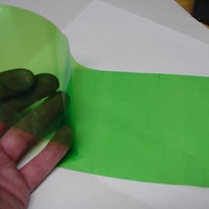 May include: A flexible, translucent lime green sheet of material with a smooth, glossy finish. The sheet is partially lifted, revealing its thin, pliable nature and vibrant, semi-transparent color quality against a plain white surface.