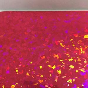 K&ouml;nnte beinhalten: Ein Bogen rotes holografisches Papier mit einem verstreuten Muster aus bunten, unregelm&auml;&szlig;igen Formen. Die Formen sind haupts&auml;chlich gelb, orange und lila und erzeugen einen schimmernden Effekt. Das Papier ist oben leicht gebogen.