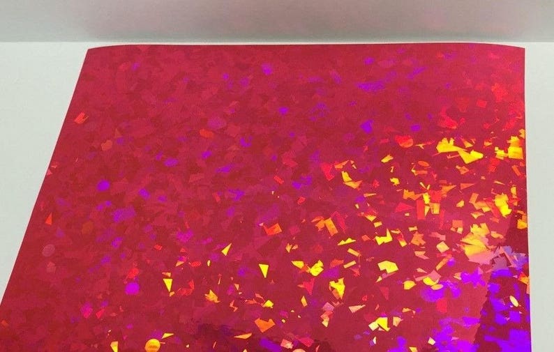 K&ouml;nnte beinhalten: Ein Bogen rotes holografisches Papier mit einem verstreuten Muster aus bunten, unregelm&auml;&szlig;igen Formen. Die Formen sind haupts&auml;chlich gelb, orange und lila und erzeugen einen schimmernden Effekt. Das Papier ist oben leicht gebogen.