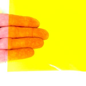 May include: A rectangular sheet of translucent yellow plastic film. The material is smooth and flexible, allowing light to pass through while tinting the view of objects behind it with a vibrant, bright yellow color across the entire surface.
