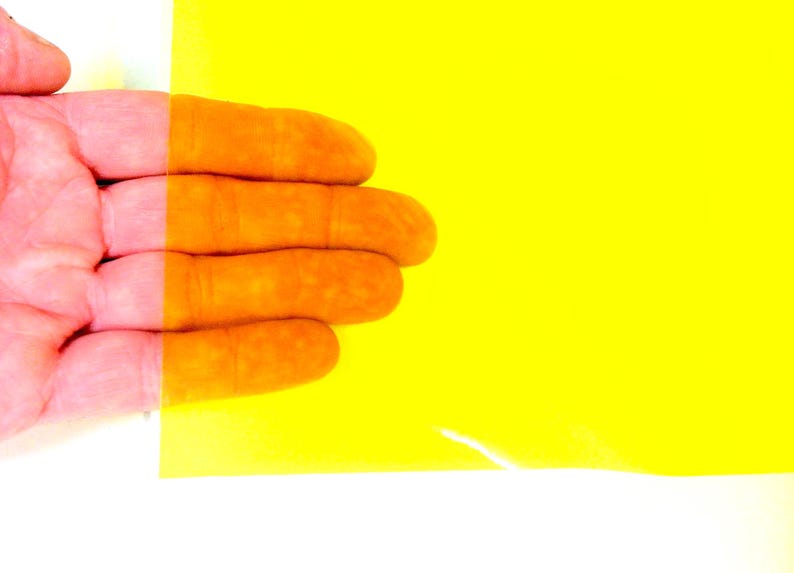 May include: A rectangular sheet of translucent yellow plastic film. The material is smooth and flexible, allowing light to pass through while tinting the view of objects behind it with a vibrant, bright yellow color across the entire surface.