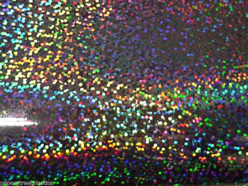 May include: A close-up of iridescent silver fabric with a holographic finish. The fabric is covered in small, round, multi-coloured sequins.