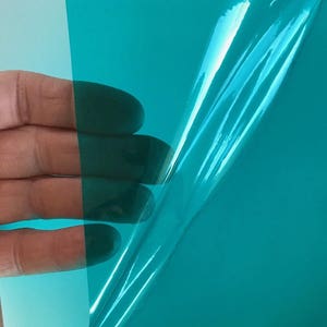 May include: A flexible, translucent sheet of teal-colored plastic film. The material is smooth, glossy, and semi-transparent, allowing light to pass through while maintaining a vibrant, consistent teal hue across its entire surface area.