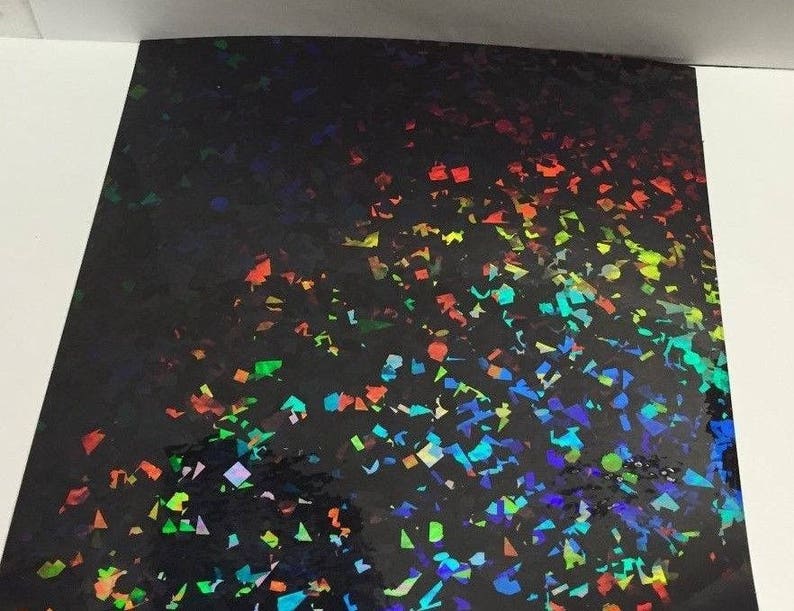 K&ouml;nnte beinhalten: Ein Bogen schwarzes holografisches Papier mit einem konfettiartigen Muster aus bunten, irisierenden Formen. Die Formen reflektieren einen Regenbogen aus Farben, darunter Rot, Orange, Gelb, Gr&uuml;n, Blau und Violett.