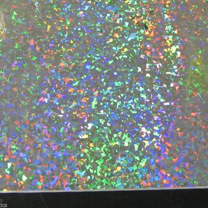 K&ouml;nnte beinhalten: Eine Folie aus schillerndem Kunststoff mit einem Streumuster aus bunten, unregelm&auml;&szlig;igen Formen. Die Farben umfassen Gr&uuml;n, Blau, Rot und Gelb und erzeugen einen schimmernden Effekt. Das Material ist reflektierend.