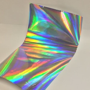 May include: A sheet of iridescent holographic vinyl with a rainbow pattern. The vinyl is folded in half and has a slight curve.