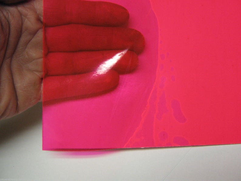 May include: A translucent, vibrant hot pink plastic sheet with a smooth, glossy finish. The material is flexible and semi-transparent, allowing light to pass through while casting a bright pink hue over the surface beneath it.