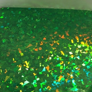 K&ouml;nnte beinhalten: Ein Blatt gr&uuml;nes holografisches Papier mit einem Konfetti-&auml;hnlichen Muster. Die reflektierende Oberfl&auml;che schimmert in verschiedenen Farben, darunter Gr&uuml;n, Gelb und Orange. Das Papier ist rechteckig und hat eine gl&auml;nzende Oberfl&auml;che.