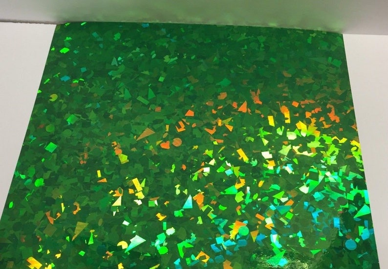 K&ouml;nnte beinhalten: Ein Blatt gr&uuml;nes holografisches Papier mit einem Konfetti-&auml;hnlichen Muster. Die reflektierende Oberfl&auml;che schimmert in verschiedenen Farben, darunter Gr&uuml;n, Gelb und Orange. Das Papier ist rechteckig und hat eine gl&auml;nzende Oberfl&auml;che.