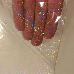 May include: A sheet of clear iridescent holographic vinyl with a scattered pattern of small, multi-colored dots.
