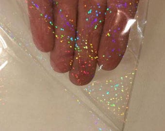 Pode incluir: Uma folha de vinil holográfico transparente e iridescente com um padrão disperso de pequenos pontos multicoloridos.