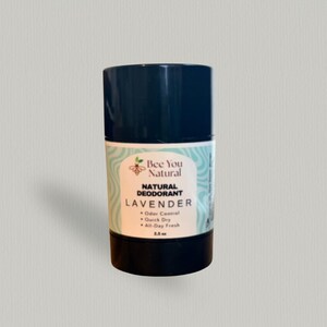 Puede incluir: Un desodorante en barra cilíndrico negro con una etiqueta que dice Bee You Natural, Natural Deodorant, Lavender, Odor Control, Quick Dry, All-Day Fresh, 71g. La etiqueta presenta un pequeño icono de abeja y un fondo de patrón ondulado azul claro.