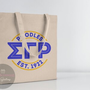 May include: A beige canvas tote bag with blue and gold lettering. The lettering reads "Poodles &Sigma;TP Est. 1922".