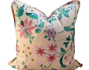 May include: A decorative pillow with a peach-colored background and a floral pattern. The design features pink, red, and yellow flowers with green leaves and vines. The pillow is square-shaped.