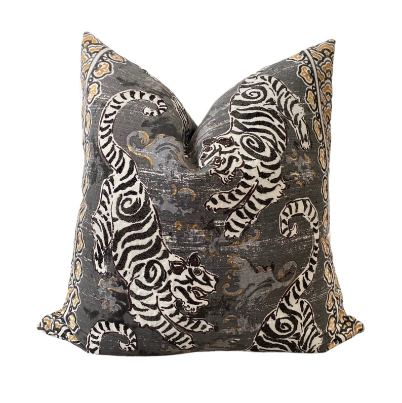 May include: A gray throw pillow with a white and black tiger print. The pillow has a gold and brown border.