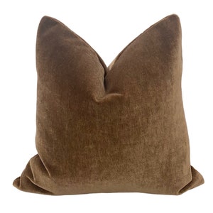 May include: A brown velvet cushion with a square shape and a smooth, soft texture.