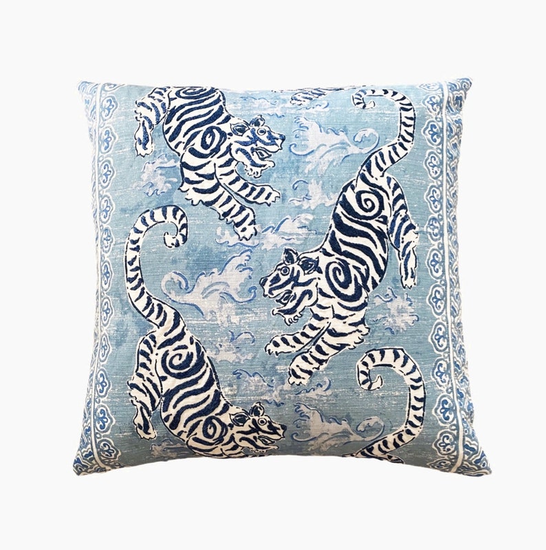 May include: A blue and white throw pillow with a repeating pattern of tigers and clouds. The pillow has a decorative border.