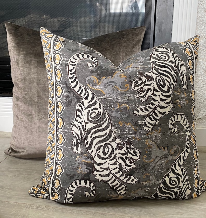 May include: A gray and white patterned throw pillow with a design of tigers. The pillow has a yellow and black border.