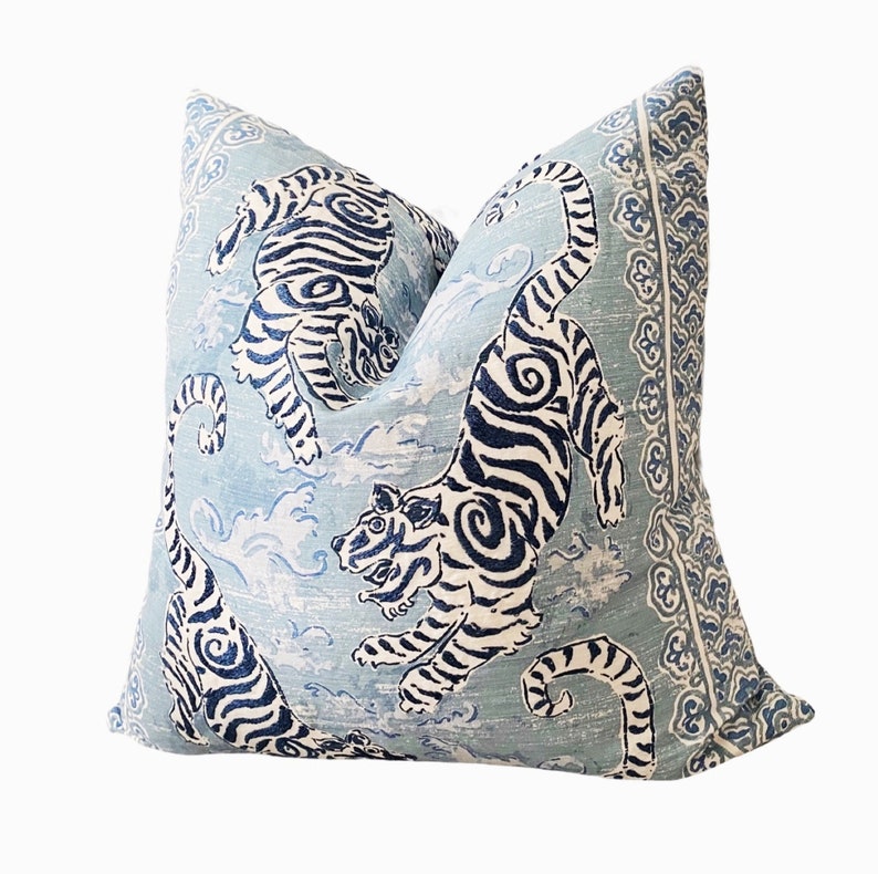 May include: A blue and white throw pillow with a pattern of tigers and clouds. The pillow has a decorative border.