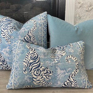 May include: Three decorative throw pillows with a blue and white tiger print. The pillows are arranged on a light wood floor. The pillow in the back is a solid light blue color.