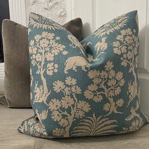 May include: A teal blue throw pillow with a beige floral and animal print. The pillow features a repeating pattern of trees, birds, and animals.