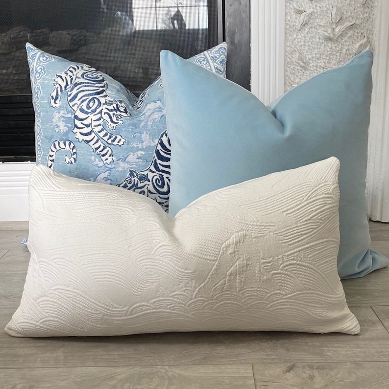 May include: Three decorative throw pillows. One pillow is white with a raised wave pattern. One pillow is light blue with a white and blue tiger pattern. One pillow is light blue with a white and blue floral pattern.