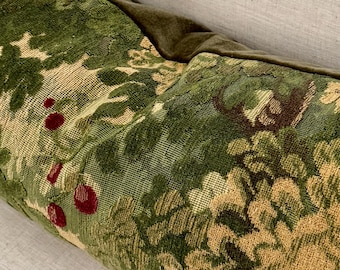 May include: Close-up of a decorative pillow with a green and tan floral pattern. The pillow features a tapestry design with accents of red berries. The top edge is a dark green velvet.