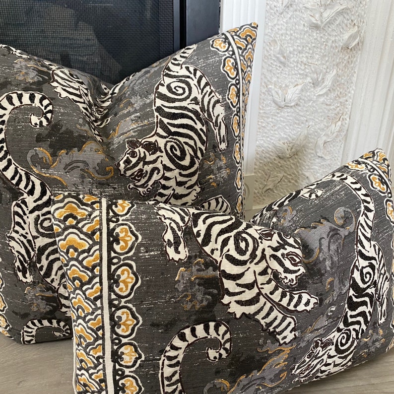 May include: Two decorative throw pillows with a gray background and a white and black tiger print. The pillows have a gold and white border with a floral design.