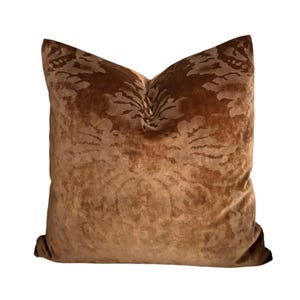 May include: A square, brown velvet pillow with a floral pattern. The pillow has a soft, plush appearance and is a warm, inviting color. The floral design is subtly visible across the surface.