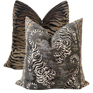 May include: Two decorative throw pillows with a tiger print. One pillow is a brown and black tiger print on a velvet fabric. The other pillow is a gray and white tiger print on a linen fabric.
