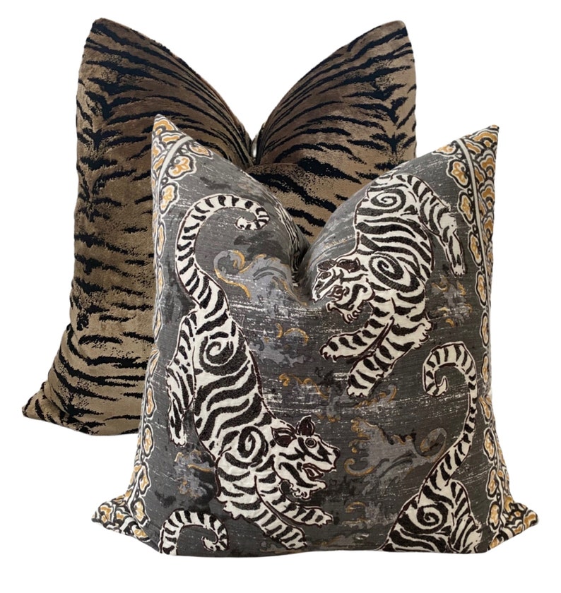 May include: Two decorative throw pillows with a tiger print. One pillow is a brown and black tiger print on a velvet fabric. The other pillow is a gray and white tiger print on a linen fabric.