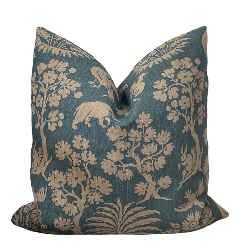 May include: A teal blue throw pillow with a beige floral and animal print. The print features trees, birds, and a rhinoceros.