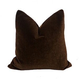 May include: A dark brown decorative pillow with a soft, velvety texture. The pillow is square-shaped and has a classic design, perfect for adding a touch of elegance to any living space. The pillow is made of a plush material.