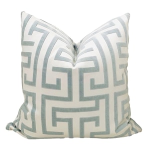 May include: A white throw pillow with a light blue geometric pattern. The pattern is a repeating design of interlocking squares and rectangles.