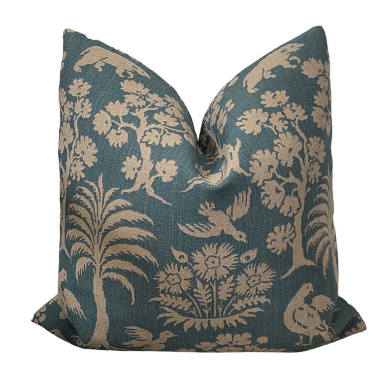 May include: A teal blue throw pillow with a beige floral and bird pattern. The pillow is made of a soft, textured fabric.