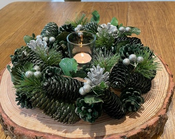 Christmas table centrepiece decoration with a real log slice stand, green foliage and dried cones, sparkly silver cones and baubles