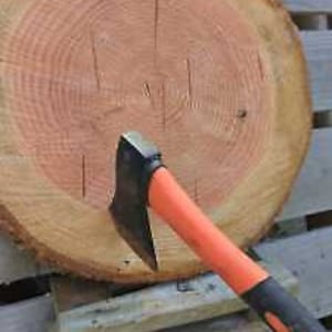 May include: A black and orange axe with a wooden handle is stuck into a round wooden target. The target has a natural wood grain pattern.