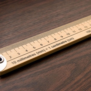 May include: A wooden ruler with black markings for centimetres and millimetres. The ruler has a metal end cap with a hole in it. The text on the ruler reads "10 millimetres (mm) = 1 centimetre (cm)" and "100 centimetres".