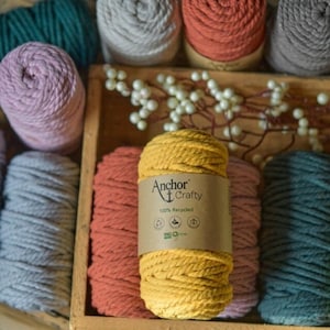 May include: A close-up of a yellow cotton rope with a label that reads "Anchor Crafty 100% Recycled". The rope is surrounded by other cotton ropes in various colors, including gray, pink, red, and green.