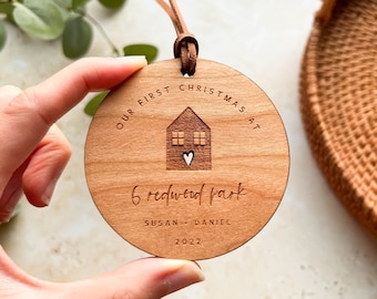May include: A round wooden ornament with the text "Our First Christmas At 6 Redwood Park Susan - Daniel 2022" and a small house with a heart in the center.