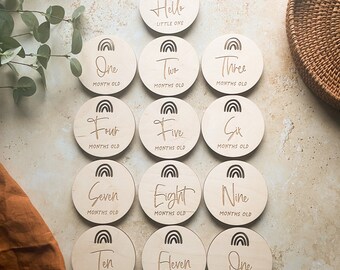 Può includere: Un set di 12 dischi in legno per le tappe del bambino con disegni arcobaleno e testo inciso. I dischi presentano le frasi "Hello Little One", "One Month Old", "Two Months Old", "Three Months Old", "Four Months Old", "Five Months Old", "Six Months Old", "Seven Months Old", "Eight Months Old", "Nine Months Old", "Ten Months Old", "Eleven Months Old" e "One Year Old".
