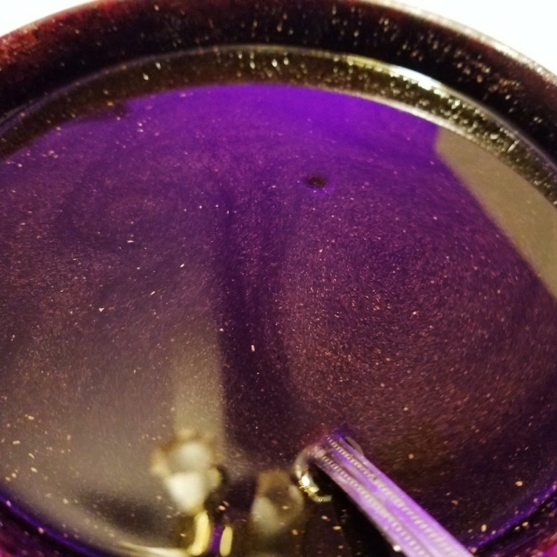 May include: A close-up of a dark purple, round, ceramic dish with a shiny, speckled surface. The dish is empty and appears to be made of glazed pottery.